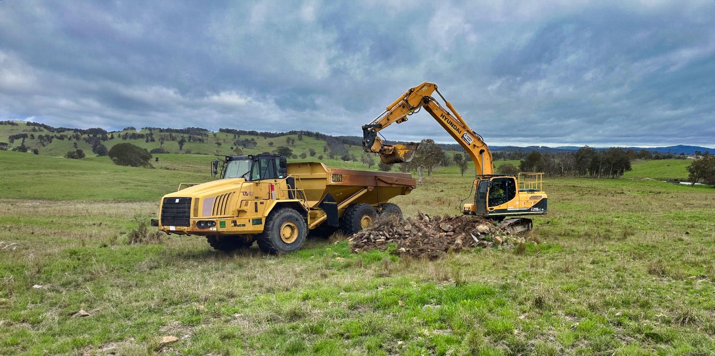 Excavator loading a dump truck in a paddock